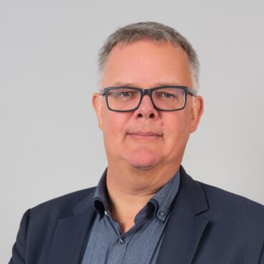 Ein Mann mit Brille posiert für ein Foto in einer Unternehmensumgebung.